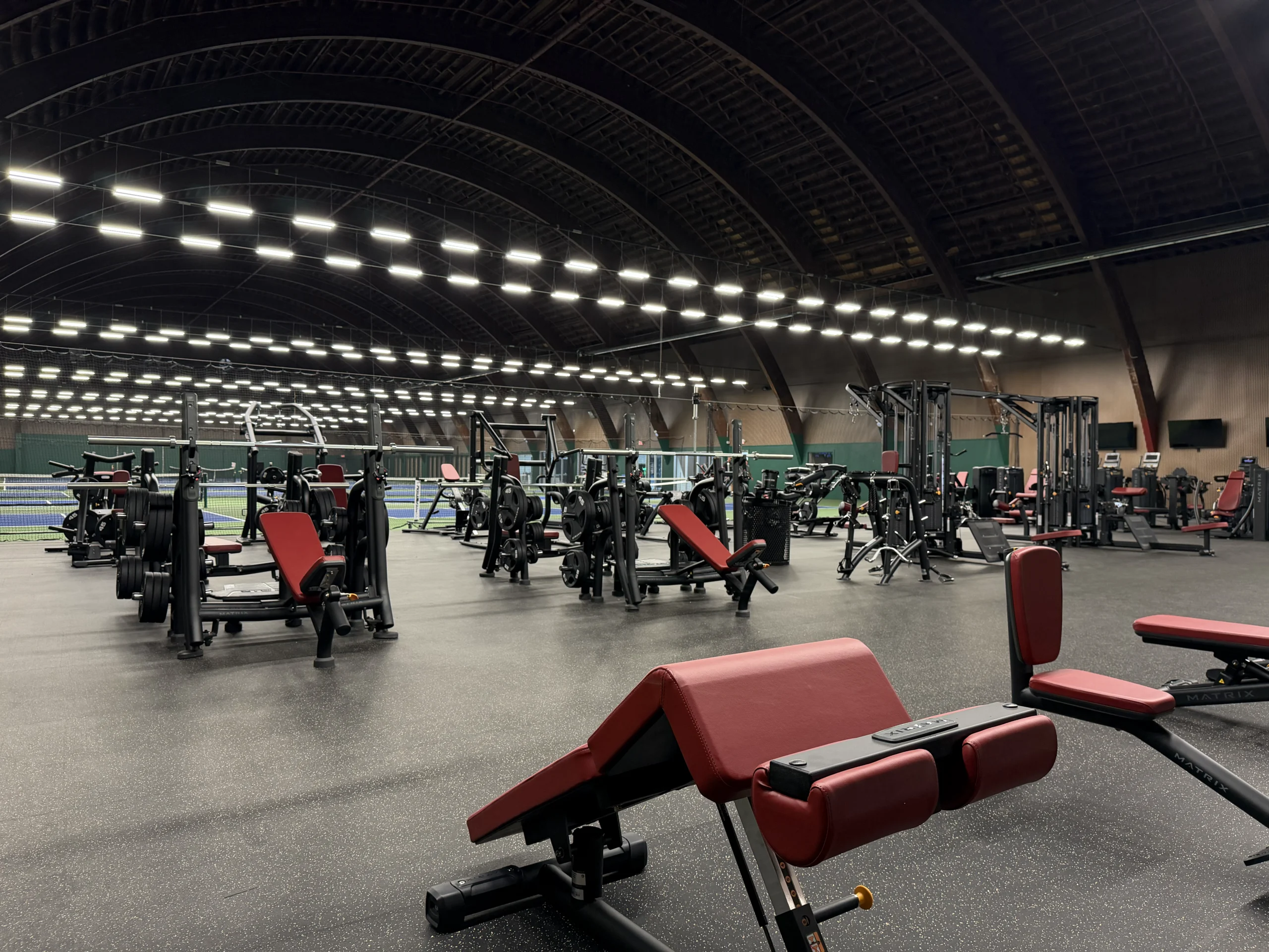 Matrix strength machines and weight benches beside the indoor courts at Grosse Ile Athletic Club